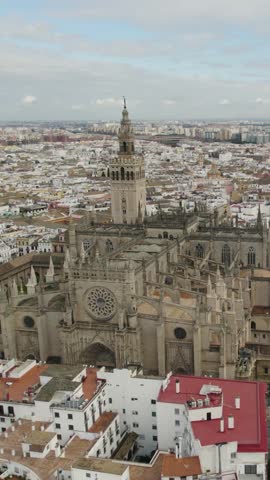 Vertical aerial orbit showcasing Seville Cathedral and its surrounding historic rooftops.