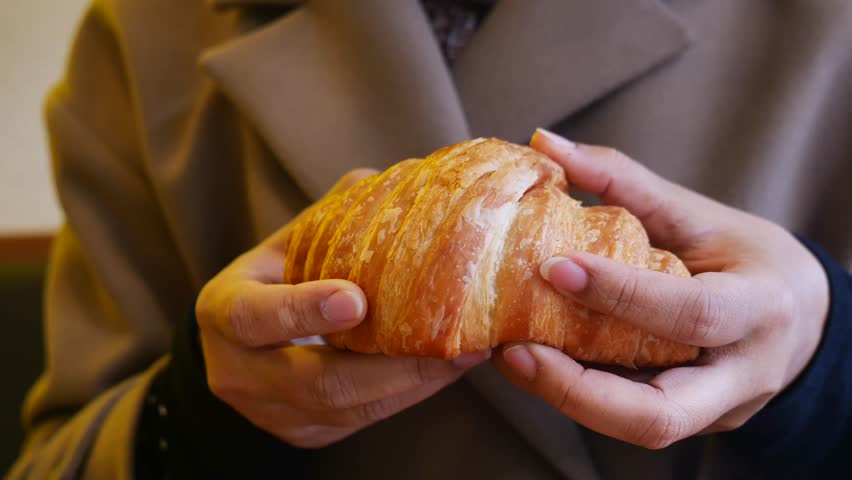 Woman hands breaking fresh flaky croissant in slow motion showing soft buttery layers and delicious texture