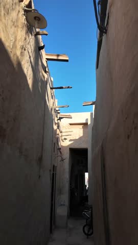Walking through narrow ancient alley in historic Souq Waqif with traditional architecture and vibrant blue sky