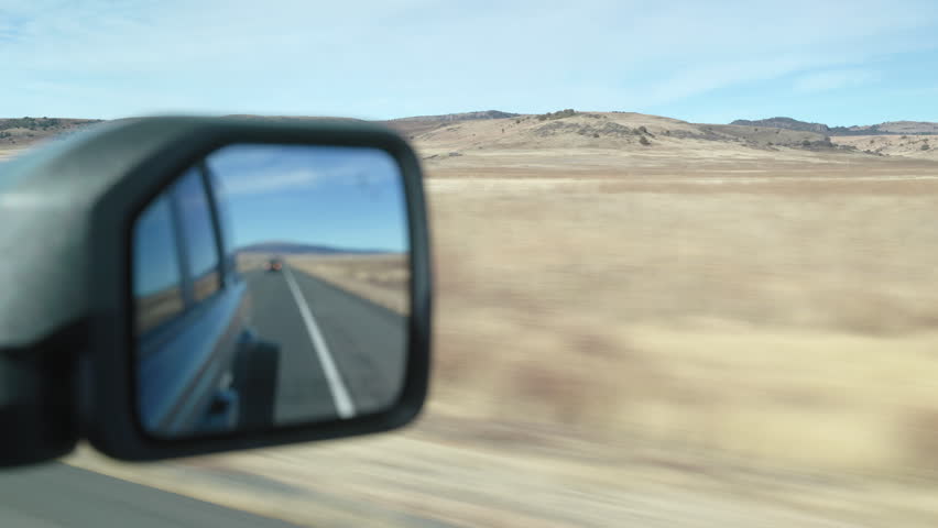 Passengers POV looking in to the rear view mirror while driving along a New Mexico highway in the desert