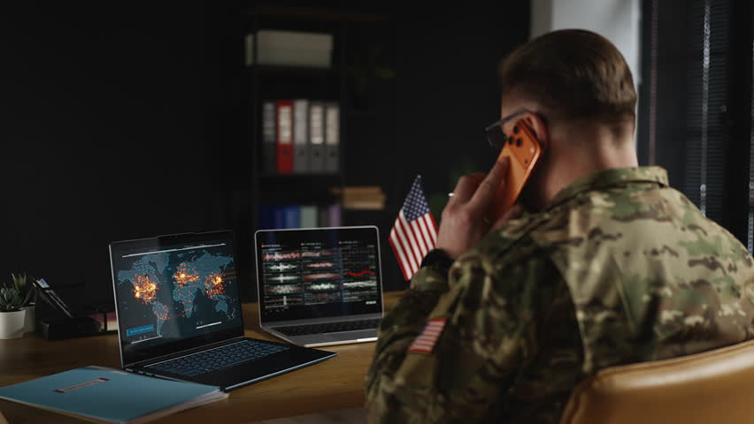 U.S. army officer talking phone while monitoring international armed conflicts