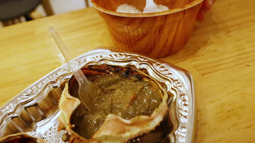 Close-up shot of hands using a plastic spoon to mix kani miso into white rice