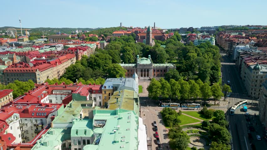 Forward aerial flyover tracking Gothenburg University grand neoclassical facade surrounded by Vasaparken lush canopy with Vasa kyrka and city rooftops visible behind