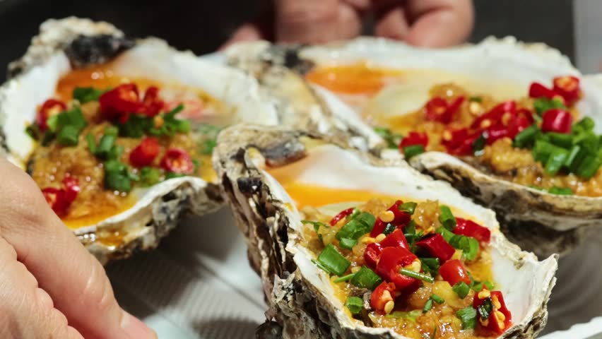 Close-up of hands holding a tray of oysters garnished with red and green chilies.