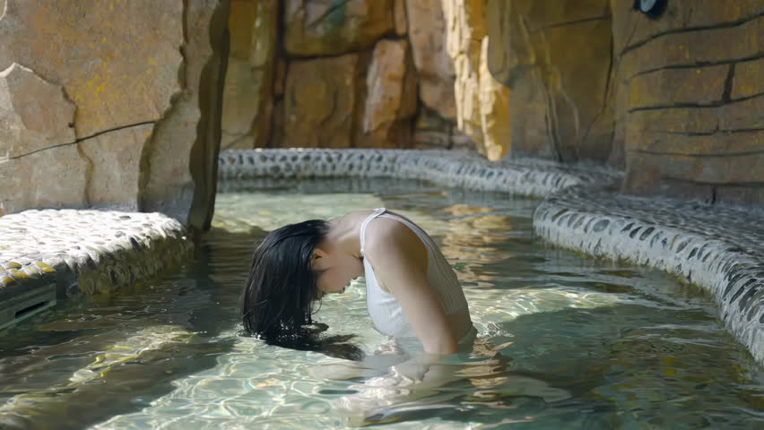 Beautiful young woman relaxing in a natural hot spring spa, swing long hair enjoys traditional onsen in open hot thermal swimming pool at sunrise for wellness travel and spa tourism industries