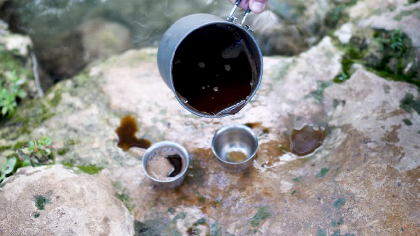 Top view of coffee poured into camping cups on rock near river.