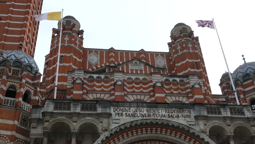 Westminster Cathedral facade in London with red and white brick pattern, towers and flags. Upward view showing entrance and architectural details