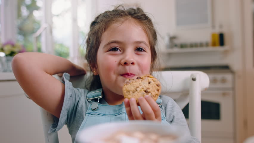 Happy, child and eating cookies in home for sweet treat, homemade snack and comfort food on weekend. Smile, girl kid and enjoy biscuit in kitchen for baked goods, chocolate chip dessert and hungry