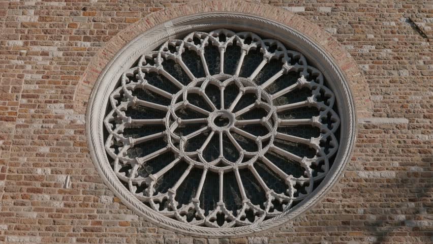 Close up of the intricate stone rose window of the Cathedral of San Giusto in Trieste Italy showing gothic architectural details and brick wall on a sunny day