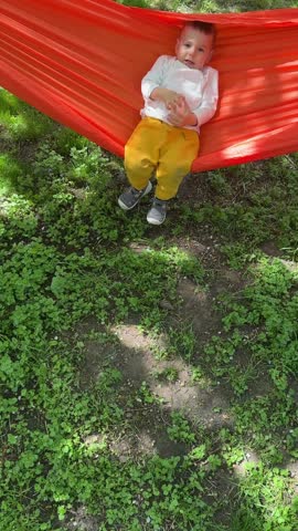 Sleeping baby relaxing in orange hammock outdoors.