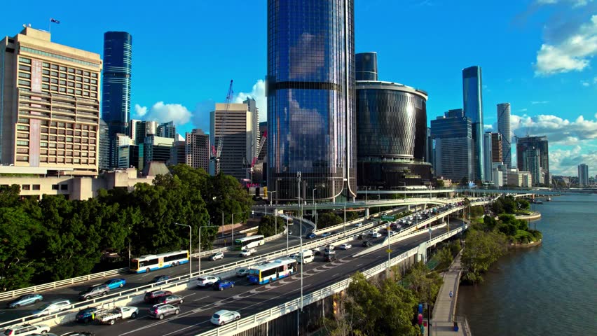 Aerial cityscape of Brisbane CBD, Queensland, Australia, with Riverside Expressway traffic, modern glass skyscrapers, and the Brisbane River under bright blue skies.