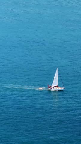Aerial footage of sailboat sailing on a deep blue sea with white waves