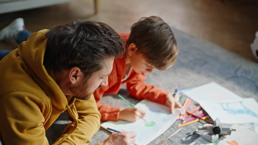 Father son drawing floor using colorful pencils involved art hobby together closeup. Smiling bearded man talented little boy enjoy creative sketching at carefree home leisure. Childhood activity.