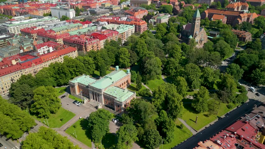 Ascending aerial pulls back over Vasaparken revealing Gothenburg University neoclassical building, Vasa kyrka church and sweeping orange-roofed residential cityscape in summer