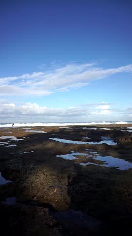 Coastal view with rocky shore and ocean waves under a bright blue sky, showcasing natural seaside beauty.