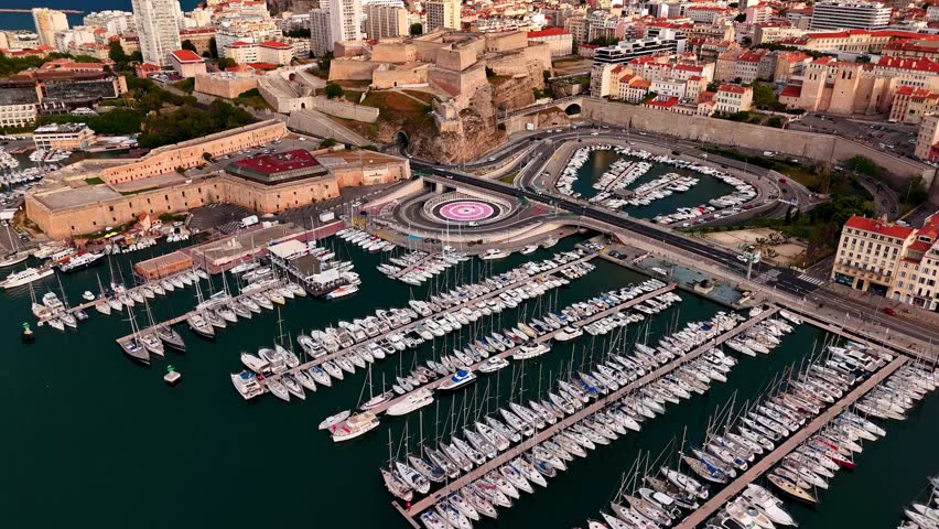 Aerial drone view of Marseille’s Vieux-Port marina and Fort Saint-Nicolas, featuring docked yachts, historic fortifications, curved roadways, and the waterfront cityscape of southern France.