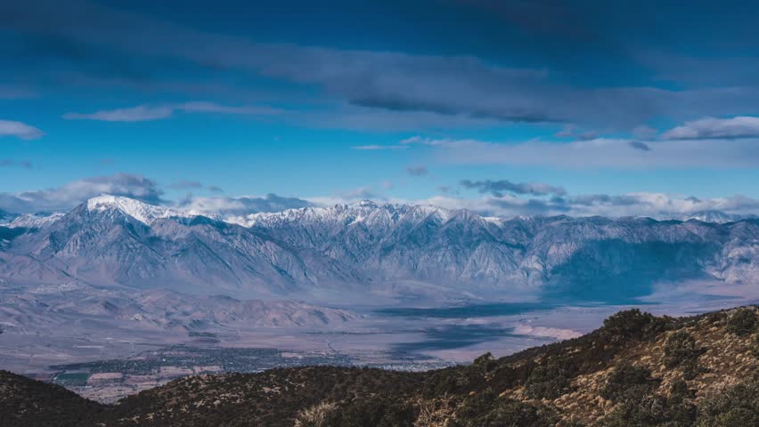 This 4K video captures a panoramic view of the High Sierra Mountains in California. The visual documents snow-covered granite peaks and rocky alpine terrain of the Sierra Nevada range. The composition illustrates the contrast between high elevations and the eastern valley floor, documenting glacial geomorphology and cold-weather atmospheric conditions for nature and editorial media.