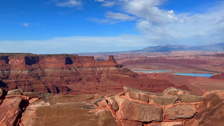 This 4K video captures an overlook at Dead Horse Point State Park, Utah. The visual documents rock formations aged between 184 and 285 million years. The composition illustrates bright blue solar evaporation ponds used for potash mining near Canyonlands National Park, documenting Colorado Plateau geology and industrial land use for nature and editorial media.