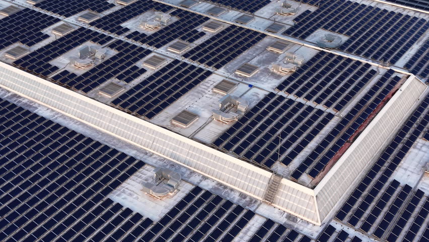 Large rooftop photovoltaic system with grid-tied solar panels, inverters, mounting racks and HVAC units on industrial building for distributed power generation