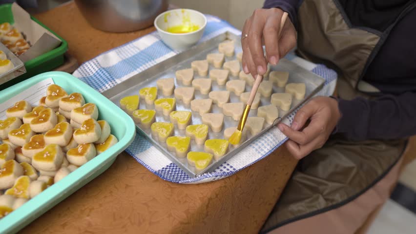 Woman Brushing Egg Wash on Heart-Shaped Cookies Before Baking