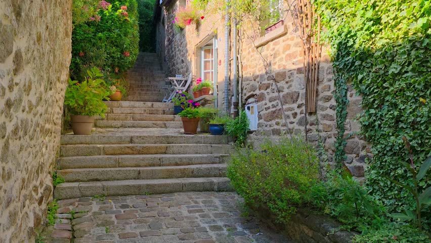 Beautiful flower filled steeped street in the picturesque Old Town of Dinan, Brittany, France during summer. Slow upward panning motion.
