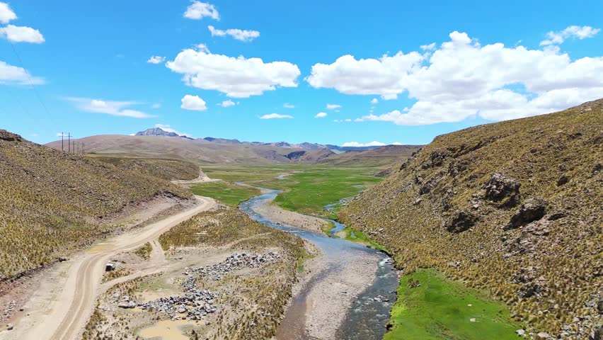 Aerial drone view of green landscapes, wetlands, rivers, and rural villages in the Peruvian Andes. High-altitude mountains, natural scenery, and countryside roads in a remote Andean environment.