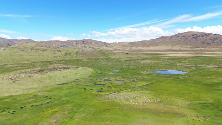 Aerial drone view of green landscapes, wetlands, rivers, and rural villages in the Peruvian Andes. High-altitude mountains, natural scenery, and countryside roads in a remote Andean environment.