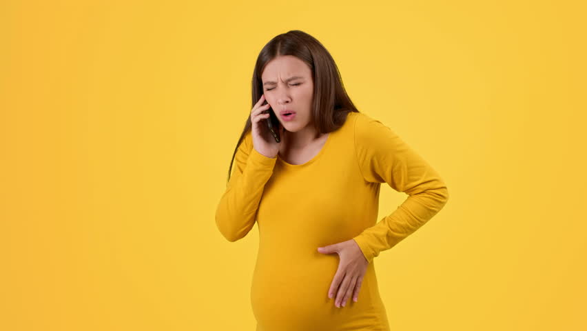 Pregnant Woman With Brown Hair Talks on the Phone While Experiencing Discomfort