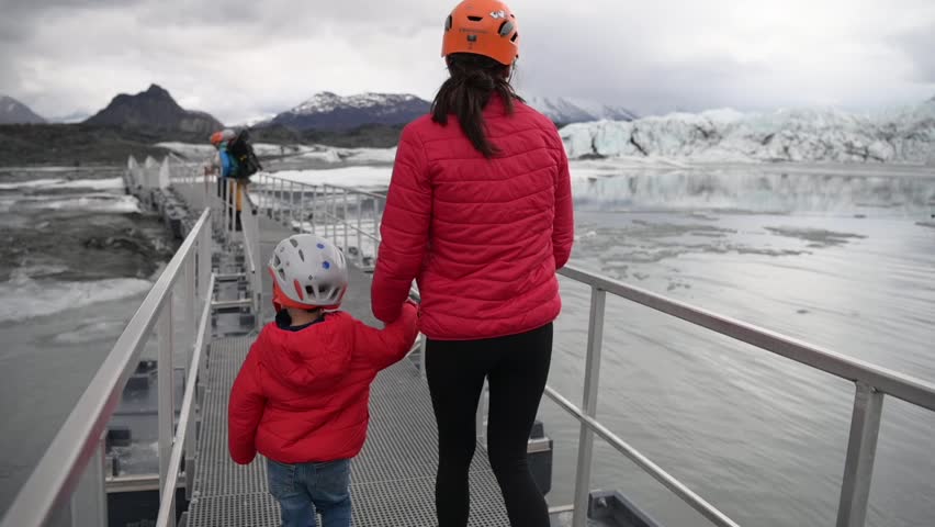 Group hiking across a glacier bridge in Alaska, wearing helmets and crampons, including a child.  Scenic mountain landscape and icy terrain visible.  Ideal for travel, adventure, and outdoor projects. 