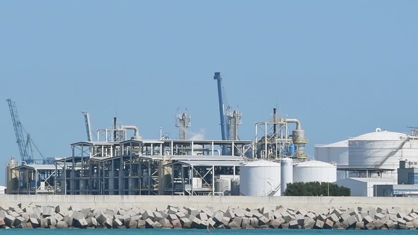 Smoky oil refinery complex, metal structures, storage tanks on a pier with breakwaters, close up. Marine terminal for receiving and distributing oil from tankers. War Iran, Kuwait, Strait of Hormuz, Kharg Island