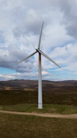 Wind turbines stand on a rocky, dry hill under a cloudy sky, representing sustainable power