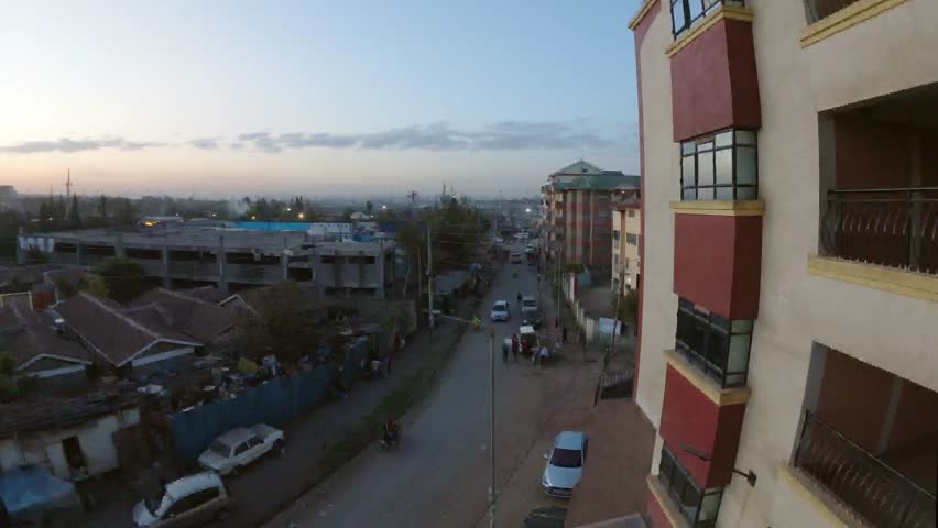 Timelapse of dusk traffic in a Nairobi residential neighborhood. Elevated view highlights apartment architecture, street lighting, and urban security and accommodation in Kenya