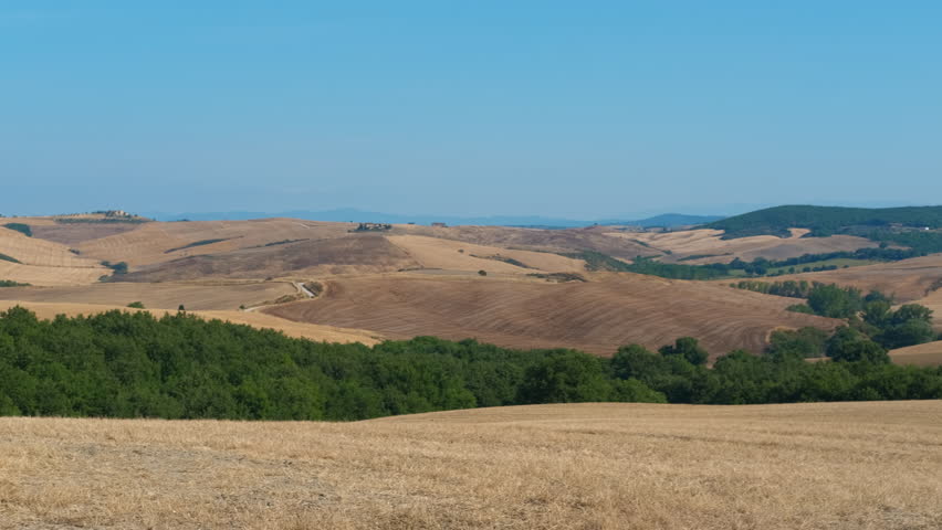 Golden hay bales in the tuscan countryside during summer. Scenic view of the golden rolling hills of tuscany, with large round hay bales in a freshly harvested wheat field under a clear blue sky