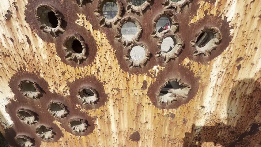 A rusted metal wall full of large bullet holes. 