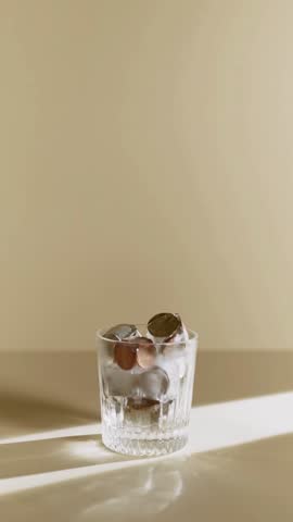 Action of pouring a golden liquor or beverage from a textured crystal bottle into a glass filled with ice cubes.