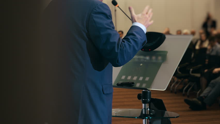 Close up of business speaker presenting at conference podium with microphone addressing audience representing public speaking leadership and corporate presentation.