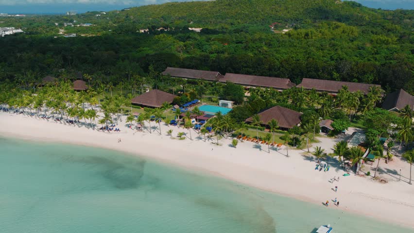Tropical beach resort with palm trees swimming pool and white sand shoreline, medium aerial orbit, Bohol Philippines