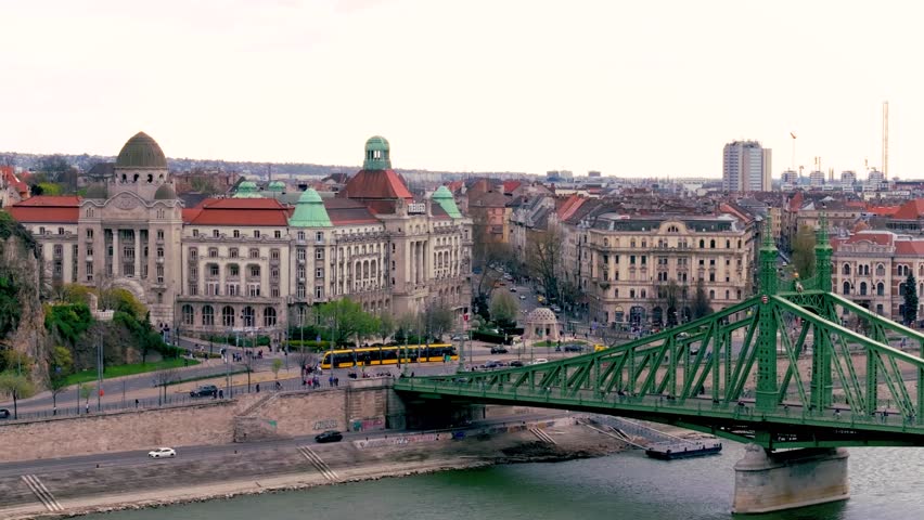 A stunning view of the szechenyi chain bridge in budapest, hungary, showcasing its intricate metalwork. Cars travel across the bridge, with the danube river flowing beneath and city buildings visible. high-quality professional detailed modern elegant stylish clean crisp vibrant colorful