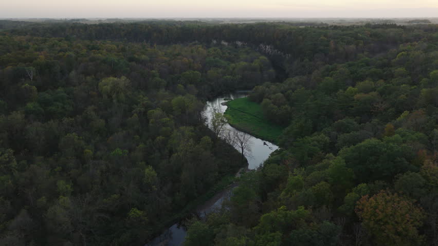 Winding Root River cutting through forest landscape in Root River Park Minnesota, aerial panoramic pullback at dusk