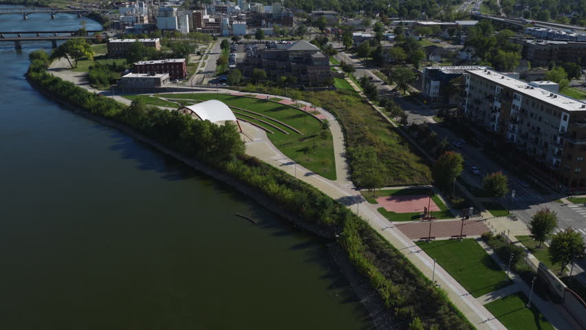 Riverside McGrath park amphitheater beside Cedar River in Cedar Rapids Iowa with walking paths and lawn, aerial dolly into downtown