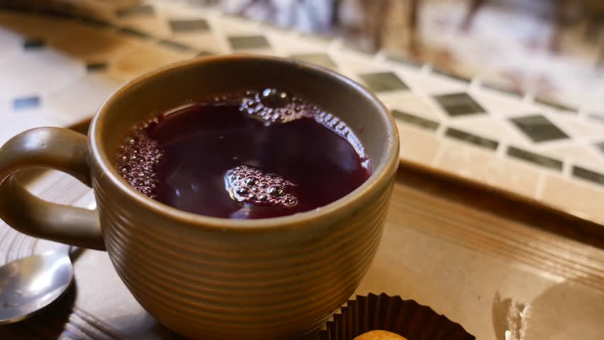 Cinematic shot of hand picking up steaming cup of hot berry tea from wooden tray in cozy cafe setting.