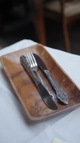 Close up of person hand picking up silver vintage knife and fork from wooden tray on white table cloth.