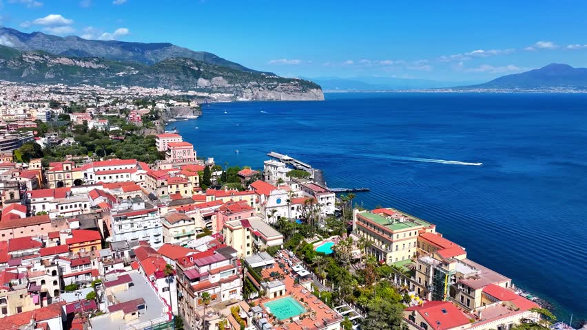 Aerial view over Sorrento on Italy’s Sorrentine Peninsula, showing Marina Piccola, cliffside hotels, terracotta rooftops, and the deep blue Bay of Naples on a bright summer day.