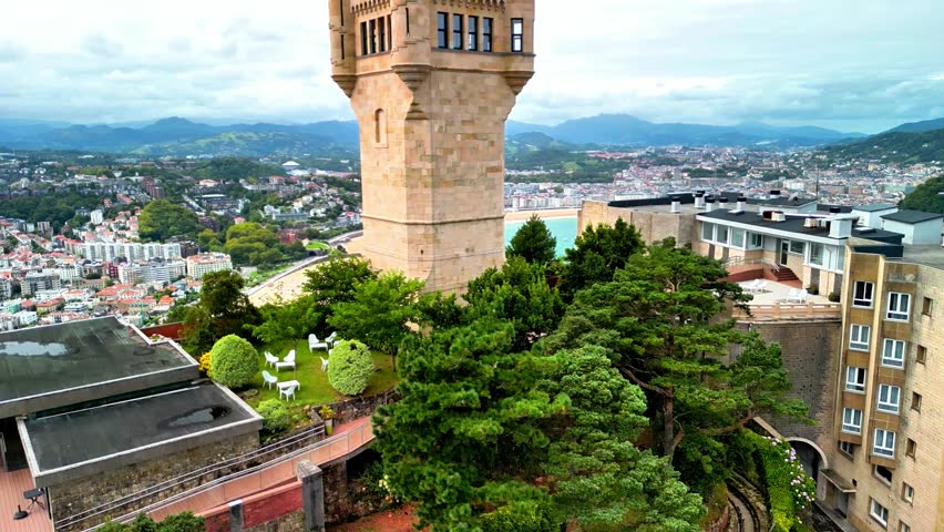 Panoramic hilltop view of the historic Torreón on Monte Igueldo overlooking La Concha Bay, San Sebastián cityscape, and sandy beach beneath dramatic clouds in the Basque Country, Spain.
