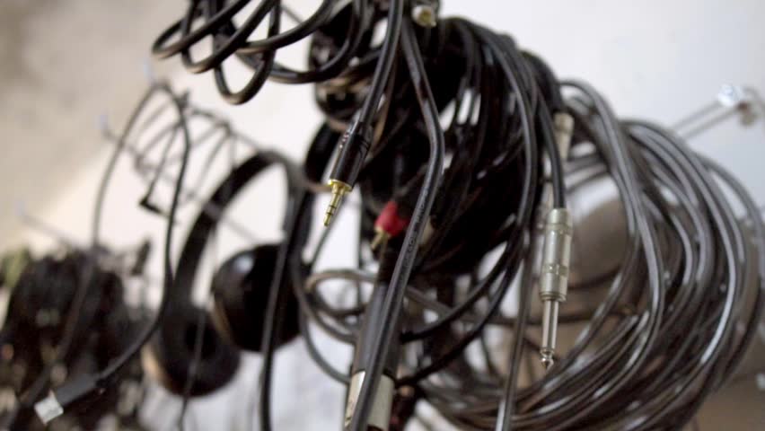 Close up of various tangled audio cables, jack connectors, and headphones hanging in a music recording studio.