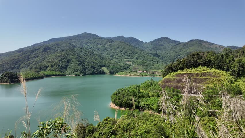 Scenic landscape of a vast emerald lake nestled between lush green mountains and hills under a clear blue sky.