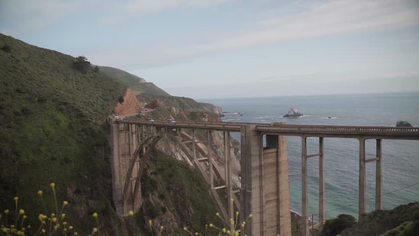 Elevated view of the iconic arch bridge spanning a coastal canyon with steep green cliffs and open ocean in the background. Big Sur, California, Big Sur, California