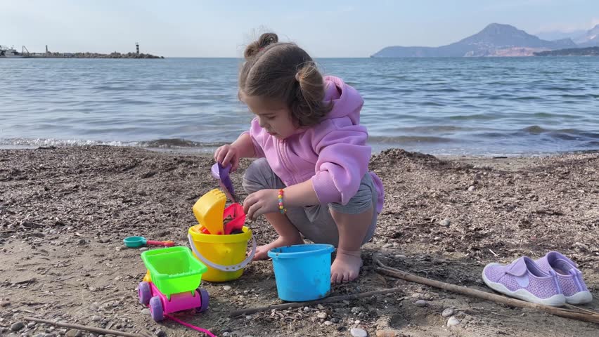 Cute baby girl playing with toy car and shovel on yellow sand on the beach by Adriatic sea