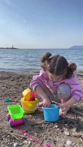 Cute baby girl playing with toy car and shovel on yellow sand on the beach by Adriatic sea