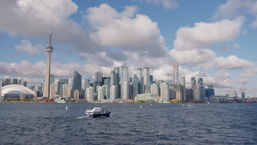 Boat cruising on Lake Ontario with Toronto skyline in background, wide view of modern cityscape and waterfront under dramatic clouds.
